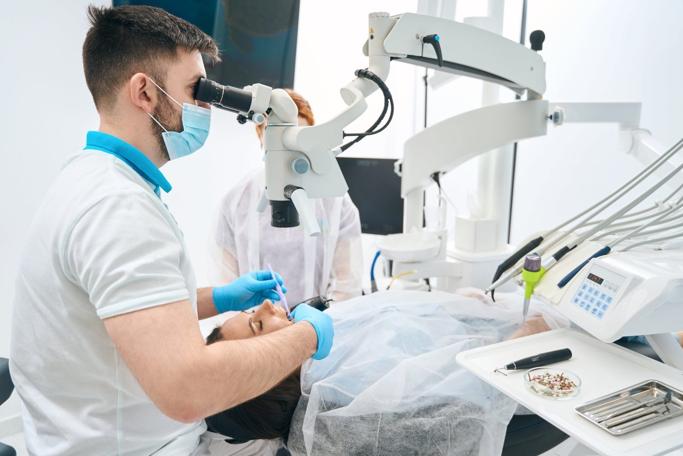 A dentist works through a dental microscope while a nurse assists